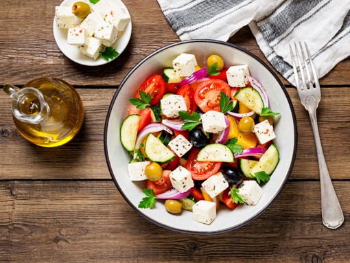 Das Gericht "Griechischer Bauernsalat" schön in einer Schüssel arrangiert auf einem Holztisch