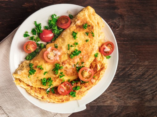 Das Frühstücksgericht "Pikantes Kräuter-Omelette" mit Tomaten schön angerichtet auf weißem Teller auf Holztisch