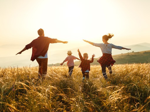 Stoffwechsel testen: Paar mit zwei Kinder läuft mit ausgebreiteten Armen über eine Wiese im Sonnenuntergang