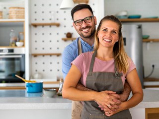 Junges Paar mit Kochschürzen steht lächelnd in der Küche